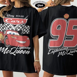 Może przedstawiać: Czarna koszulka z Lightning McQueen z filmu Auta Disneya Pixara. Prz&oacute;d przedstawia samoch&oacute;d z napisem "Lightning McQueen" i logo Cars. Tył pokazuje duży napis "95" i "Lightning McQueen" w kolorze białym.
