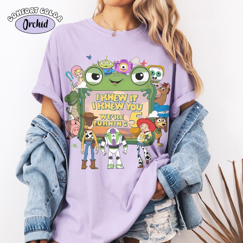 Puede incluir: Una camiseta de color morado claro con un estampado gr&aacute;fico de varios personajes animados que rodean un marco verde con forma de rana. El texto dentro del marco dice I KNEW IT I KNEW YOU WE'RE TURNING 5. La camiseta tiene mangas cortas.