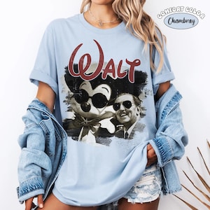 Puede incluir: Camiseta azul claro con un gr&aacute;fico de Mickey Mouse y Walt Disney en blanco y negro, con el nombre "Walt" en escritura roja. La camiseta est&aacute; etiquetada como "Comfort Color Chambray".