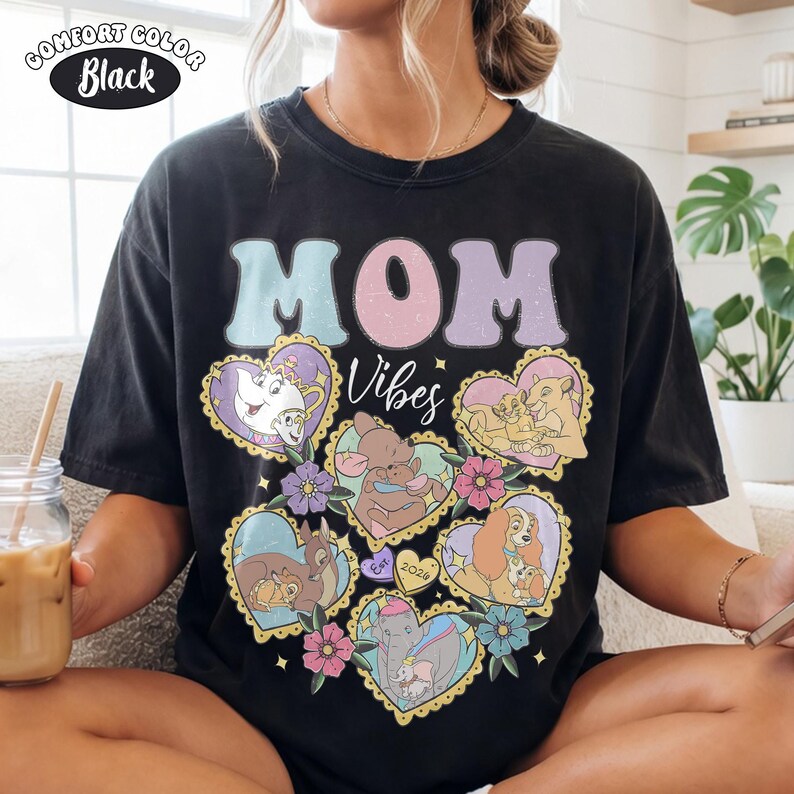 Pu&ograve; includere: T-shirt nero Comfort Colors con le parole "MOM Vibes" in colori pastello. La maglietta presenta illustrazioni a forma di cuore di personaggi Disney. La maglietta ha un aspetto vintage e usurato.