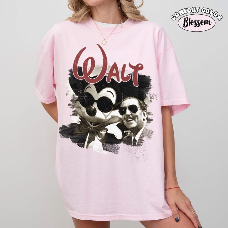 Puede incluir: Camiseta rosa claro con un gr&aacute;fico en blanco y negro de Mickey Mouse y Walt Disney con gafas de sol, con la palabra "Walt" en escritura granate. La camiseta tiene un logotipo de "Comfort Color Blossom".