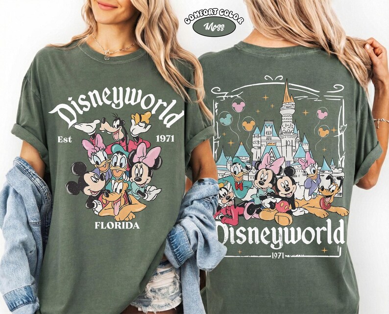 K&ouml;nnte beinhalten: Ein moosgr&uuml;nes T-Shirt mit einer Vorderseite, die den Schriftzug Disneyworld, Est 1971, Florida und Zeichentrickfiguren zeigt. Die R&uuml;ckseite zeigt ein Schloss, den Schriftzug Disneyworld 1971 und Figuren mit Luftballons in einem Rahmen.