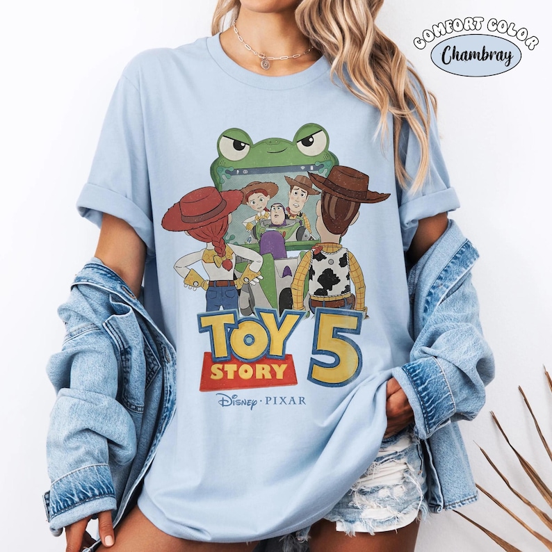 Pu&ograve; includere: T-shirt azzurra con grafica di Toy Story 5. Il design presenta personaggi come Woody, Buzz Lightyear e Jessie, con il titolo del film in evidenza. La maglietta &egrave; realizzata in materiale Comfort Colors Chambray.