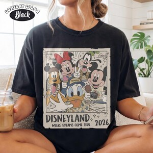 Puede incluir: Una camiseta negra con un estampado gr&aacute;fico de personajes de Disney que incluye a Mickey Mouse, Minnie Mouse, Donald Duck, Goofy y Pluto. El dise&ntilde;o incluye el texto Disneyland, Where Dreams Come True, 2026 y firmas de personajes.