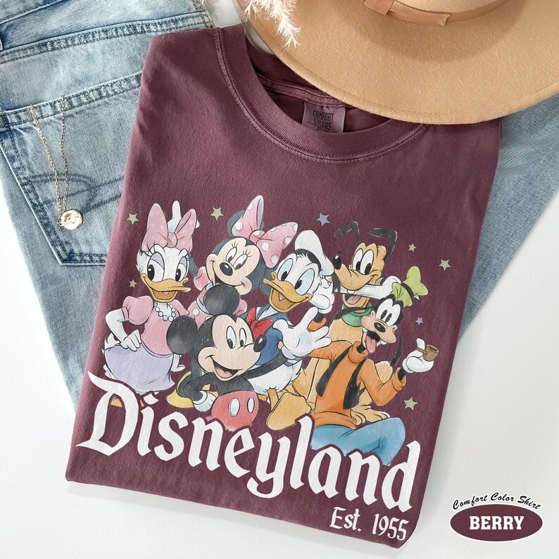 Pu&ograve; includere: Una t-shirt color bacca con una stampa grafica di Topolino, Minni, Paperino, Paperina e Pippo. Il testo Disneyland Est. 1955 &egrave; stampato sotto i personaggi. La t-shirt ha un girocollo e maniche corte.