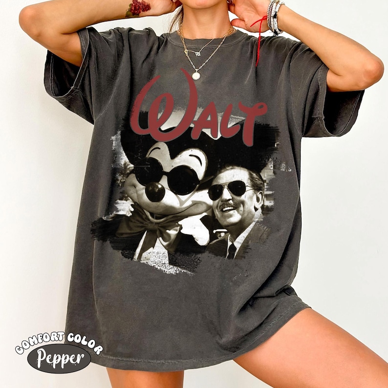 Puede incluir: Camiseta gris oscuro con un gr&aacute;fico de Mickey Mouse con gafas de sol junto a Walt Disney, con la palabra "Walt" en escritura roja. La camiseta tiene un aspecto vintage y descolorido y el texto "Comfort Color Pepper" en la parte inferior.