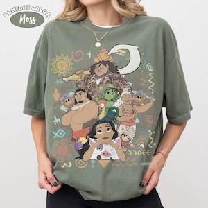 Puede incluir: Una camiseta de manga corta color verde musgo con un estampado gr&aacute;fico de personajes de la pel&iacute;cula Moana, incluyendo a Maui, Moana, Pua, Heihei y Gramma Tala, rodeados de varios s&iacute;mbolos tribales y un icono de gancho blanco.