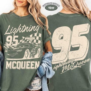 May include: Green t-shirt featuring Lightning McQueen from the Cars movie. The front design includes the text "Lightning 95 McQueen" with a graphic of the race car and a checkered flag. The back displays a large "95" and "Lightning McQueen" text.