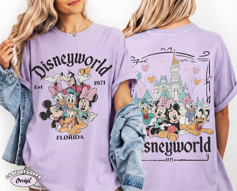 K&ouml;nnte beinhalten: Ein hellviolettes T-Shirt mit einem Grafikdruck von Disney-Figuren wie Mickey Maus, Minnie Maus, Donald Duck, Daisy Duck, Goofy und Pluto. Die Vorderseite zeigt den Text Disneyworld Est 1971 Florida. Die R&uuml;ckseite zeigt das Schloss.