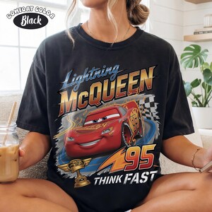 May include: Black t-shirt featuring Lightning McQueen from the Cars movie. The design includes the text "Lightning McQueen" in blue and gold, the number "95", and the phrase "Think Fast". A "Comfort Color" label is in the upper left.