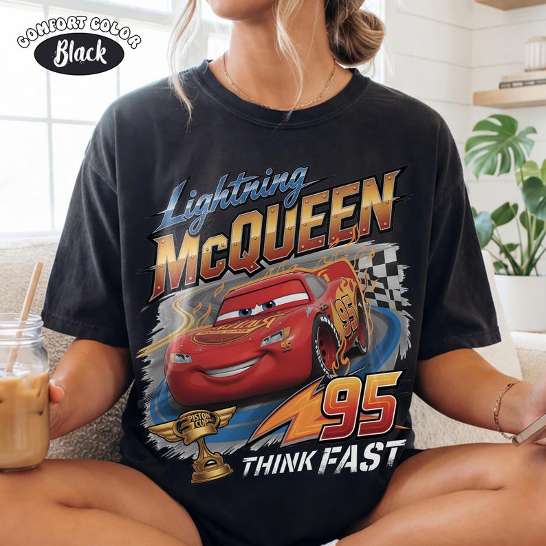 May include: Black t-shirt featuring Lightning McQueen from the Cars movie. The design includes the text "Lightning McQueen" in blue and gold, the number "95", and the phrase "Think Fast". A "Comfort Color" label is in the upper left.