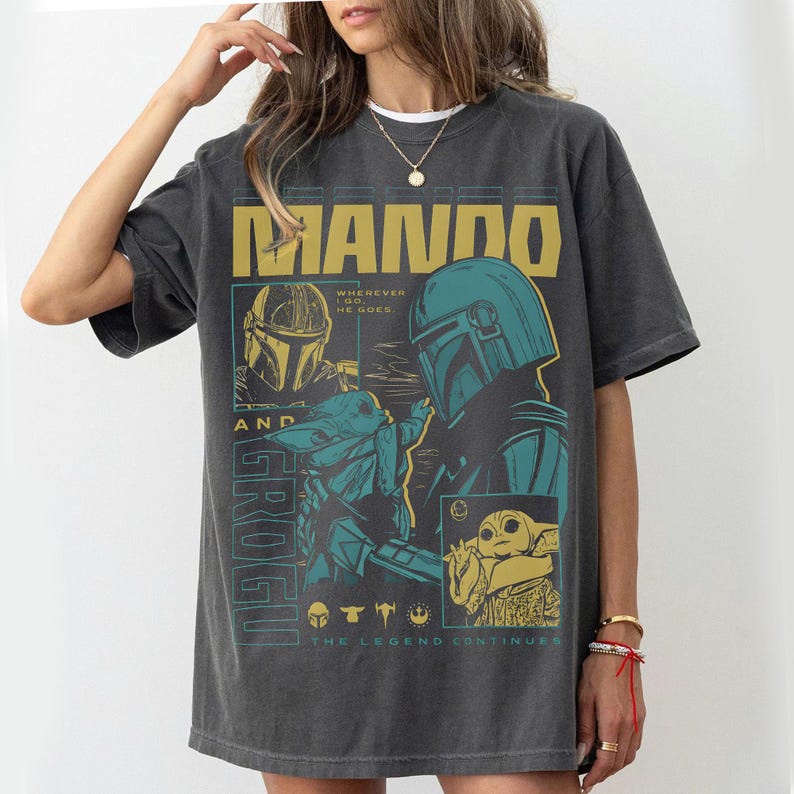 K&ouml;nnte beinhalten: Dunkelgraues T-Shirt mit einer Grafik von The Mandalorian und Grogu. Das Design enth&auml;lt den Text "MANDO" und "GROGU" sowie den Satz "WHEREVER I GO, HE GOES". Das T-Shirt hat einen Vintage-Look.