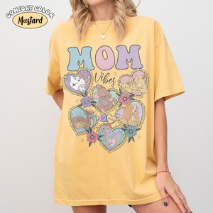 Pu&ograve; includere: T-shirt Comfort Colors giallo senape con le parole "MOM Vibes" in colori pastello. La maglietta presenta illustrazioni a forma di cuore di personaggi dei cartoni animati. La maglietta &egrave; di vestibilit&agrave; ampia.