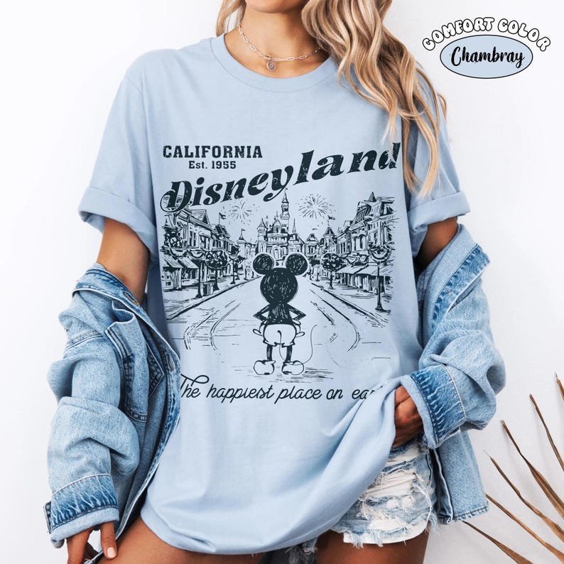 May include: Light blue t-shirt with a Disneyland graphic. The graphic features a black and white illustration of Mickey Mouse in front of a street scene with the text "CALIFORNIA Disneyland Est. 1955" and "The happiest place on earth."