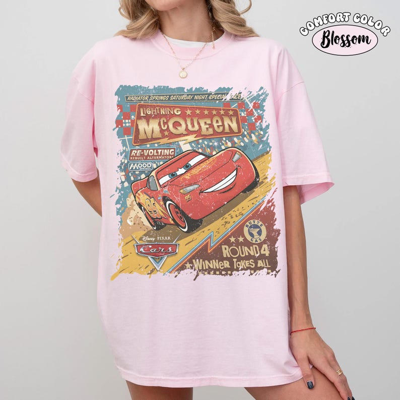 May include: A light pink Comfort Colors t-shirt featuring a distressed graphic of Lightning McQueen from the Disney Pixar Cars movie. The graphic includes text that reads "Lightning McQueen" and "Winner Takes All".