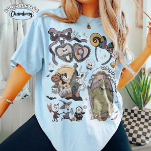 May include: A light blue t-shirt featuring a graphic print of characters and motifs from The Nightmare Before Christmas, including Jack Skellington, Sally, Oogie Boogie, Zero, and various spooky elements like pumpkins, bats, and a spiderweb.