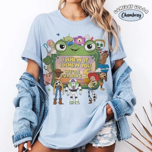 Puede incluir: Una camiseta azul claro con un estampado gr&aacute;fico de varios personajes animados que rodean un marco verde con forma de rana. El texto dentro del marco dice, I KNEW IT I KNEW YOU WE'RE TURNING 5. Un peque&ntilde;o logotipo circular indica COMFORT COLOR Chambray.