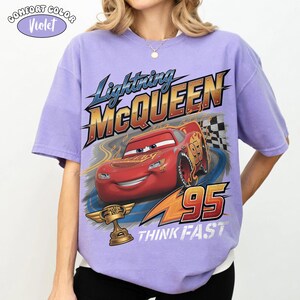 May include: Violet Comfort Colors t-shirt featuring Lightning McQueen from the Cars movie. The design includes the text "Lightning McQueen" and "95", along with a race track and the words "Think Fast".