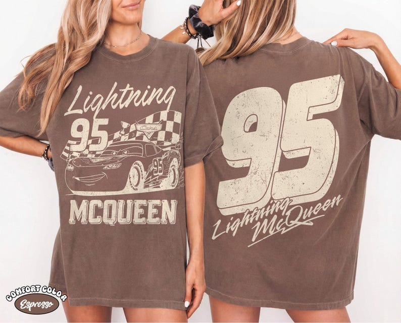 May include: Brown t-shirt featuring a graphic of Lightning McQueen from the Cars movie. The front displays the text "Lightning 95 McQueen" with a checkered flag and car illustration. The back shows a large "95" and "Lightning McQueen".