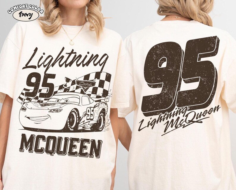May include: Ivory-colored t-shirt featuring a distressed graphic of Lightning McQueen race car with the number 95 and the text "Lightning McQueen". The back of the shirt displays a large number 95 and "Lightning McQueen".