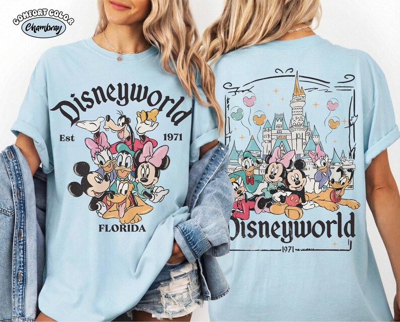 K&ouml;nnte beinhalten: Ein hellblaues T-Shirt mit einer Grafik von Disney-Figuren wie Mickey, Minnie, Donald, Daisy, Goofy und Pluto. Die Vorderseite zeigt den Text Disneyworld Est 1971 Florida. Die R&uuml;ckseite zeigt das Schloss mit dem Text Disneyworld 1971.