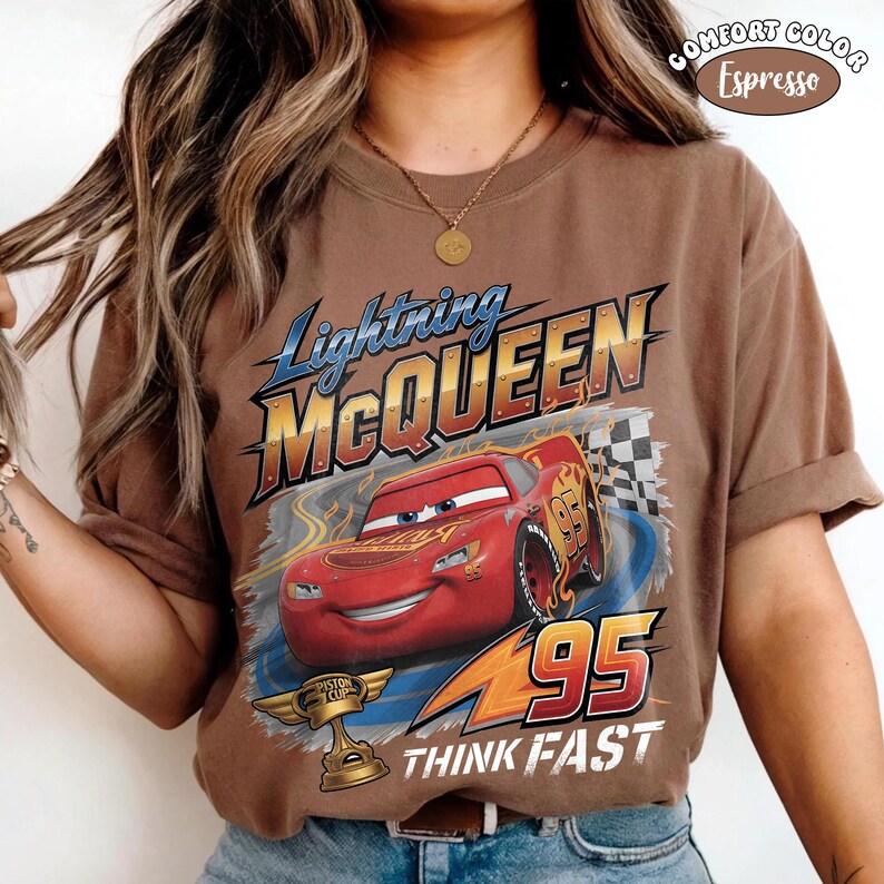 May include: Espresso-colored t-shirt featuring Lightning McQueen from the Cars movie. The graphic includes McQueen, the number 95, and the words "Think Fast." A gold trophy is also visible. The shirt is a Comfort Color.