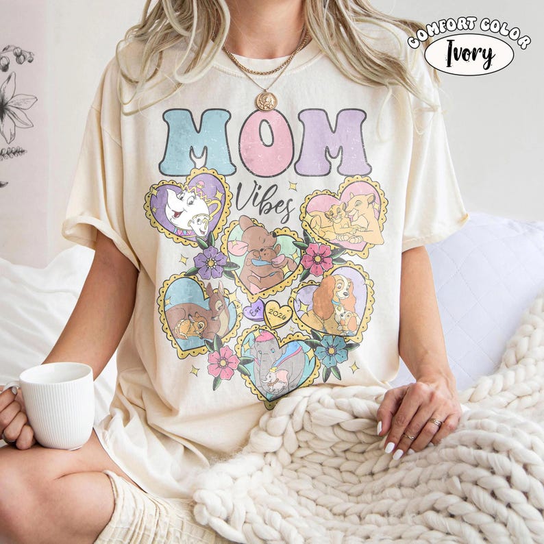 Pu&ograve; includere: T-shirt avorio Comfort Colors con le parole "MOM Vibes" in colori pastello. La maglietta presenta illustrazioni a forma di cuore di personaggi dei cartoni animati. La maglietta &egrave; a maniche corte e ha una vestibilit&agrave; ampia.