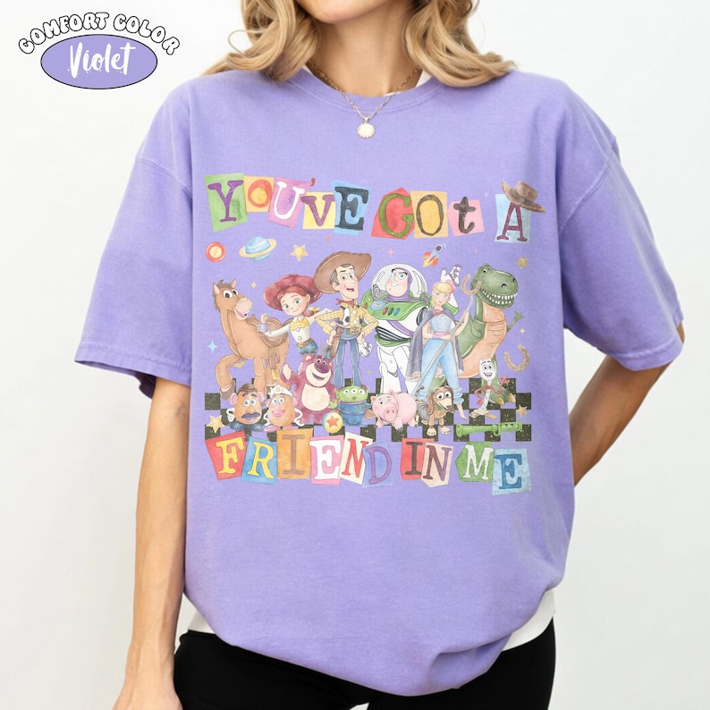 May include: A violet Comfort Colors t-shirt featuring a colorful graphic of characters from the movie Toy Story. The text "YOU'VE GOT A FRIEND IN ME" is displayed above the characters. The shirt has short sleeves and a crew neck.