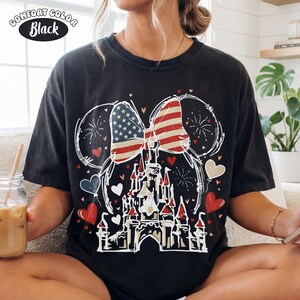 May include: Black Comfort Colors t-shirt featuring a patriotic design. The graphic includes a bow with the American flag, a castle, fireworks, and heart-shaped balloons. The text "Comfort Color Black" is in a white oval.