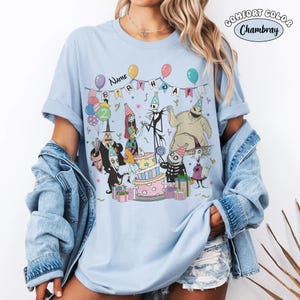 K&ouml;nnte beinhalten: Hellblaues T-Shirt mit einem Geburtstagsparty-Design mit Charakteren aus The Nightmare Before Christmas. Das Design zeigt einen Kuchen, Luftballons und den Text "NAME BIRTHDAY 2". Das Shirt besteht aus Comfort Colors Chambray-Material.