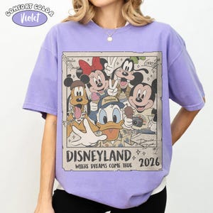 Puede incluir: Una camiseta violeta de manga corta con un estampado gr&aacute;fico de personajes de Disney que incluye a Mickey Mouse, Minnie Mouse, el Pato Donald, Goofy y Pluto. El texto dice Disneyland Where Dreams Come True 2026, con firmas de personajes.