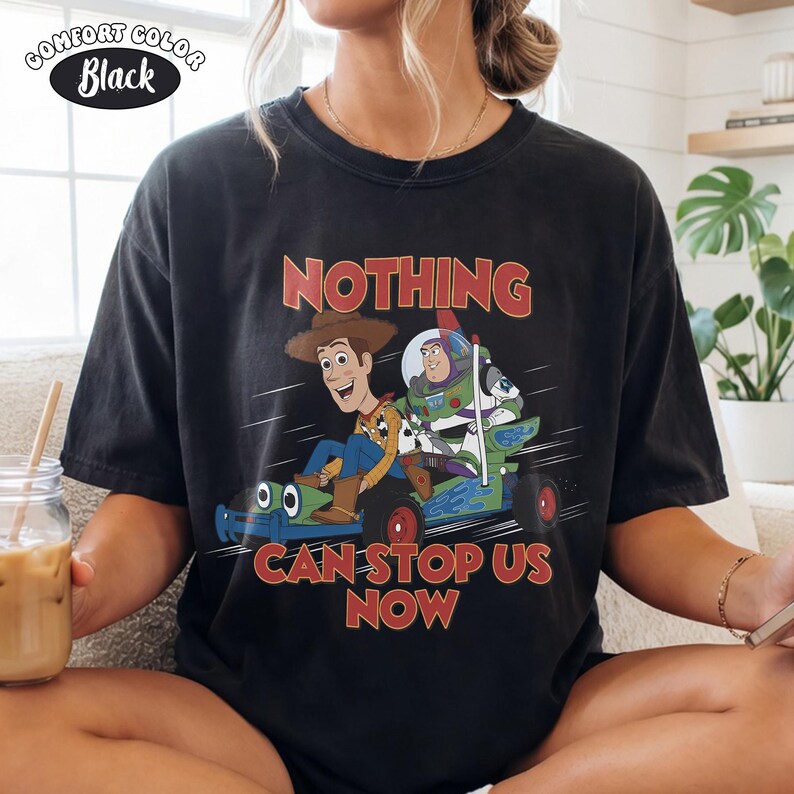 May include: Black Comfort Colors t-shirt featuring Woody and Buzz Lightyear from Toy Story. The graphic shows the characters in a race car with the text "NOTHING CAN STOP US NOW" in red. The shirt has a vintage look.