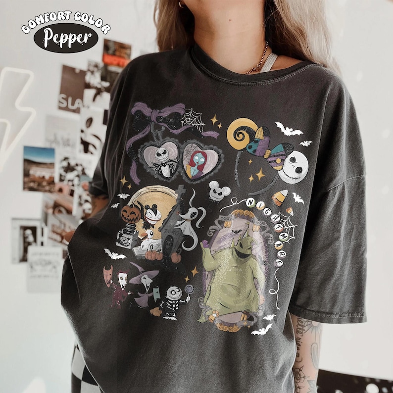 May include: A charcoal gray t-shirt featuring a graphic print of characters from The Nightmare Before Christmas, including Jack Skellington, Sally, Zero, and Oogie Boogie, along with spiderwebs, bats, and the text Comfort Color Pepper.