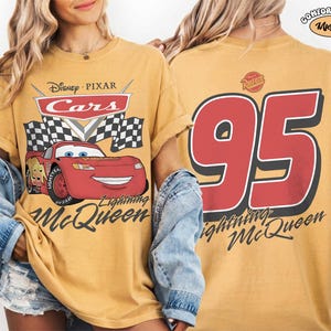 Może przedstawiać: Musztardowa koszulka z Lightning McQueen z filmu Auta Disneya Pixara. Prz&oacute;d przedstawia logo Cars, szachownicę i Lightning McQueen. Tył pokazuje dużą liczbę 95 i napis "Lightning McQueen."