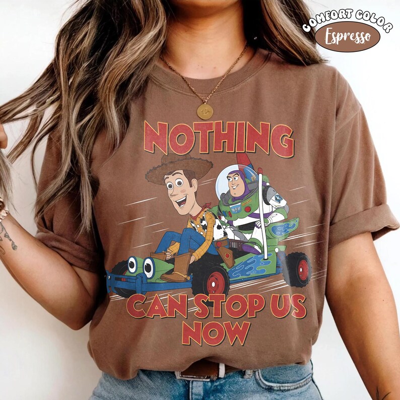 May include: Brown t-shirt with a graphic of Woody and Buzz Lightyear in a race car, with the words "NOTHING CAN STOP US NOW" in red. The shirt is labeled "COMFORT COLOR Espresso".