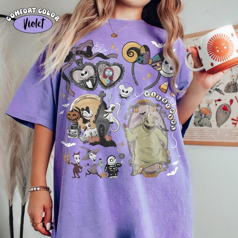 May include: A violet t-shirt featuring a graphic print of characters from The Nightmare Before Christmas, including Jack Skellington, Sally, Zero, and Oogie Boogie, alongside icons like mouse ears, pumpkins, and bats, with the text NIGHTMARE.