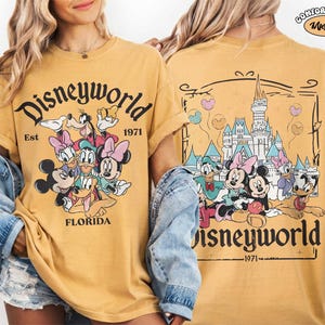 K&ouml;nnte beinhalten: Ein senfgelbes T-Shirt mit einer Grafik von Disney-Figuren, darunter Mickey Maus, Minnie Maus, Donald Duck, Daisy Duck, Goofy und Pluto. Die Vorderseite zeigt den Text Disneyworld Est 1971 Florida. Die R&uuml;ckseite zeigt das Schloss.