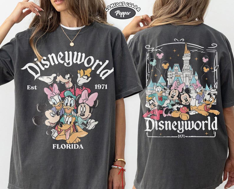 K&ouml;nnte beinhalten: Ein anthrazitfarbenes T-Shirt mit einer Grafik von Disney-Figuren wie Mickey, Minnie, Donald, Daisy, Goofy und Pluto. Die Vorderseite zeigt den Text Disneyworld Est 1971 Florida. Die R&uuml;ckseite zeigt dieselben Figuren mit einem Schloss.