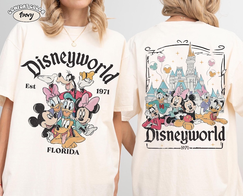 K&ouml;nnte beinhalten: Ein elfenbeinfarbenes T-Shirt mit einem Grafikdruck von Disney-Figuren wie Mickey Maus, Minnie Maus, Donald Duck, Daisy Duck, Goofy und Pluto. Die Vorderseite zeigt den Text Disneyworld Est 1971 Florida. Die R&uuml;ckseite zeigt das Schloss.