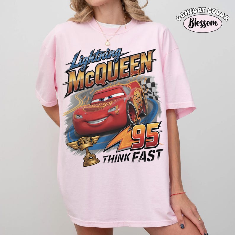 May include: Pink t-shirt featuring Lightning McQueen from the movie Cars. The graphic includes the text "Lightning McQueen", "95", and "Think Fast", along with an image of the race car and a trophy.