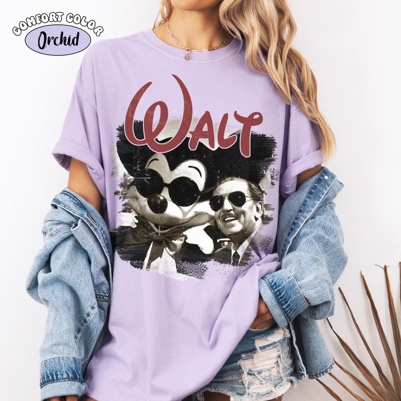 Puede incluir: Una camiseta lila Comfort Colors con un gr&aacute;fico de Mickey Mouse con gafas de sol y Walt Disney. La palabra "Walt" est&aacute; en escritura burdeos encima de la imagen. La camiseta tiene las mangas enrolladas.