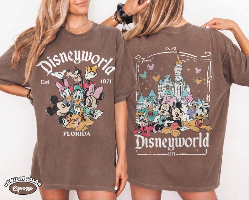 K&ouml;nnte beinhalten: Ein braunes Kurzarm-T-Shirt mit einem Grafikdruck von Disney-Figuren. Die Vorderseite zeigt Mickey, Minnie, Donald, Daisy, Goofy und Pluto mit dem Text Disneyworld Est 1971 Florida. Die R&uuml;ckseite zeigt das Schloss und die Figuren.