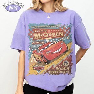 May include: Violet Comfort Colors t-shirt featuring a graphic of Lightning McQueen from the Disney Pixar Cars movie. The design includes the text "Lightning McQueen", "Radiator Springs", and "Round 4". The shirt has a relaxed fit.