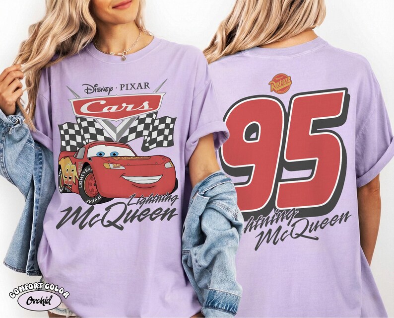 Może przedstawiać: Liliowa koszulka z Lightning McQueen z filmu Auta Disneya Pixara. Grafika z przodu zawiera logo Auta, szachownice i Lightning McQueen. Tył przedstawia dużą czerwoną liczbę 95 z imieniem Lightning McQueen.