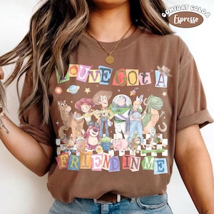 May include: Brown t-shirt with a colorful graphic featuring characters from the movie Toy Story. The text "LOVE GOT A FRIEND IN ME" is displayed above and below the characters. The shirt is labeled "Comfort Color Espresso".