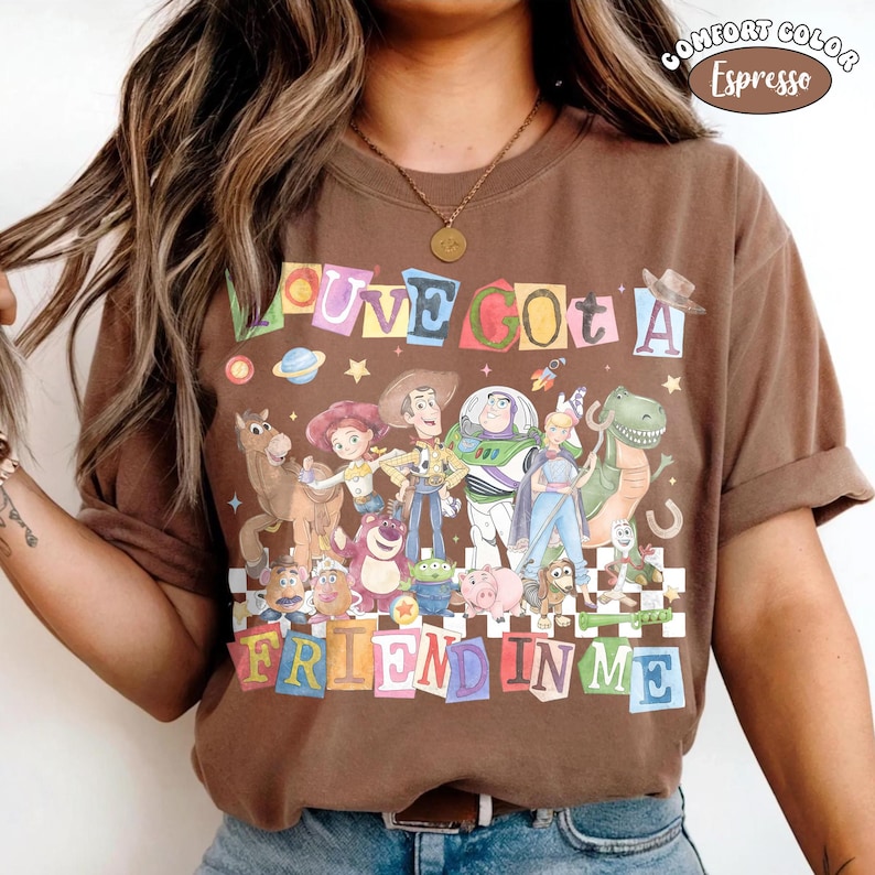 May include: Brown t-shirt with a colorful graphic featuring characters from the movie Toy Story. The text "LOVE GOT A FRIEND IN ME" is displayed above and below the characters. The shirt is labeled "Comfort Color Espresso".