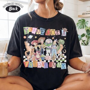 May include: Black Comfort Colors t-shirt featuring a colorful graphic of Toy Story characters. The text "YOU'VE GOT A FRIEND IN ME" is displayed above and below the characters. The shirt has a relaxed fit.