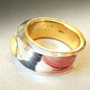 May include: A silver and gold ring with a textured design. The ring has a gold band with a silver top and a gold accent on the side. The ring is engraved with the text "NYC 212 1M71".