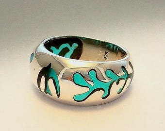 May include: A silver ring with a turquoise blue enamel design. The design features abstract shapes and swirls.