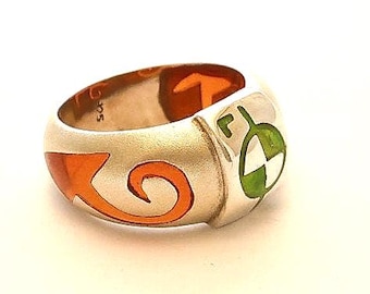 May include: A silver ring with an orange and green enamel design. The ring features a stylized arrow and a circular design with a white center.